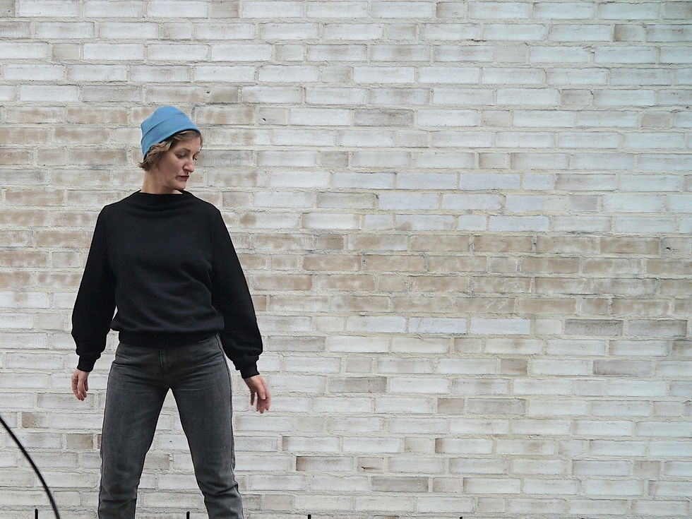 Miniaturbild: Model vor vintage weißer Backsteinwand trägt Beanie baddi in der Farbe faded blue und Sweater bon in black auf einer dunklen Jeans.