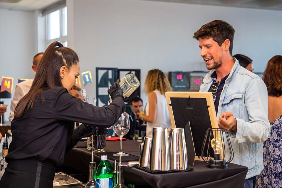 Barmaid servant un cocktail à un client souriant lors d’un événement réalisé avec un bar mobile premium à Bruxelles.