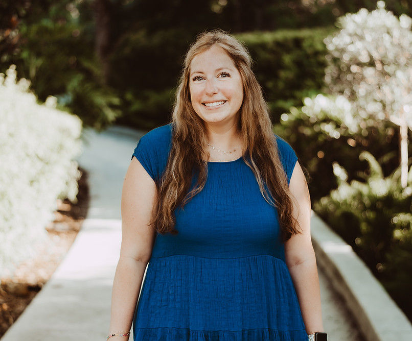 a female standing outside on a walkpath in a blue dress looking directly at the camera and smiling