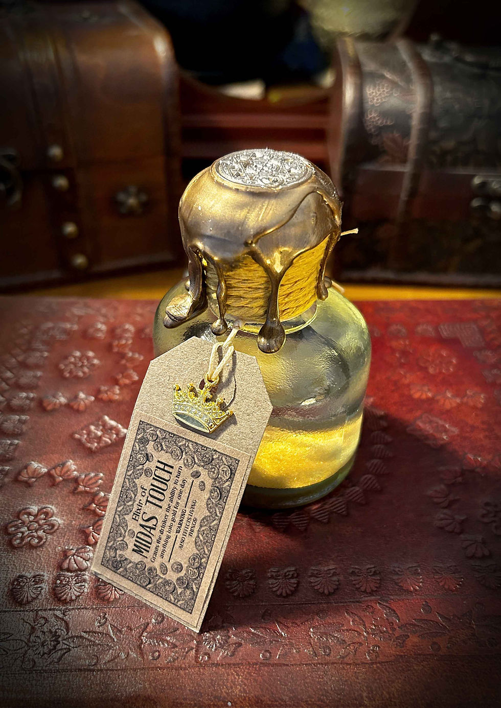 Small bottle with gold stopper, Midas Touch tag, on ornate red surface.
