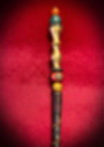 Ornate brass wand with colorful beads against a rich red background.