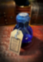 The Potion of Mana. A small, rounded glass bottle, contains a deep blue liquid. The neck is wrapped in drak blue cord and topped with a metallic blue wax, topped with a silver seal. A brown label hangs from its neck with a small silver moon charm attached.