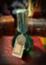 Dark green bottle, "SAGE & MYRRH" tag, melted wax, triple moon charm.