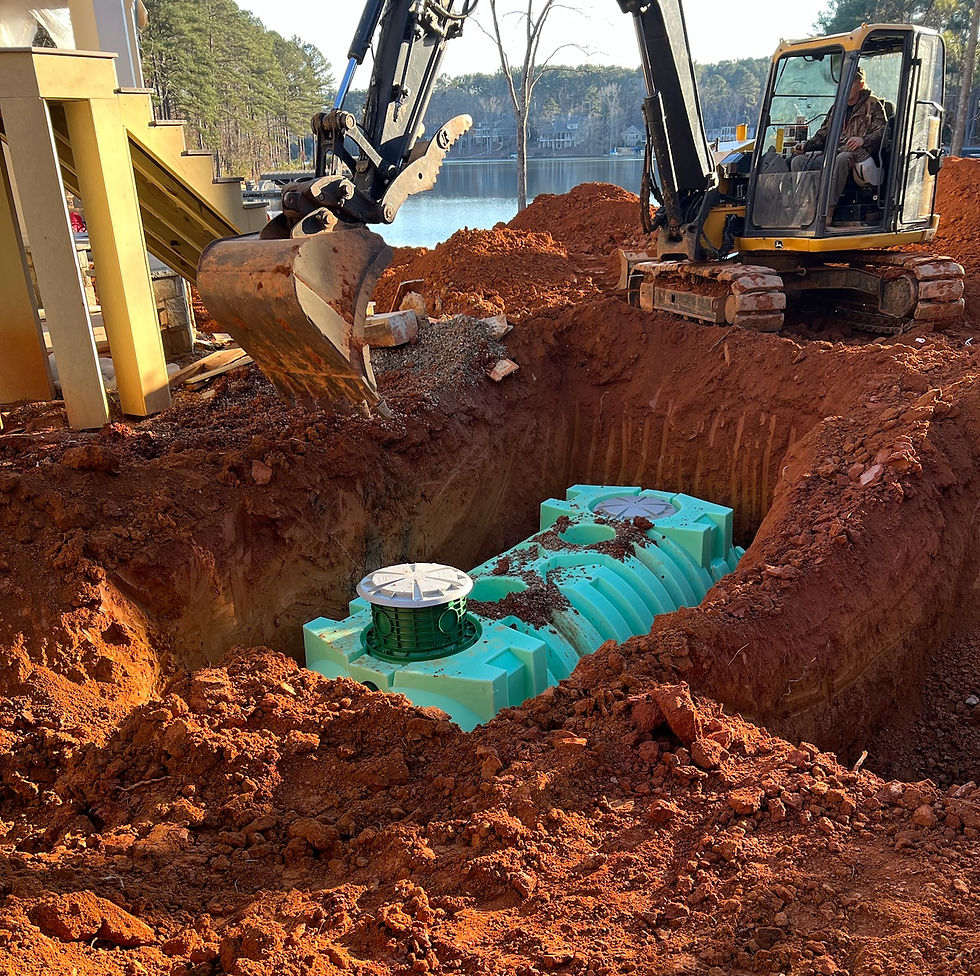 Excavator operates near a bright blue tank in a large, red-dirt pit by a lake, with trees and a wooden structure in the background.