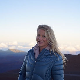 Alisha smiling on a hill top with the view of clouds in the background.