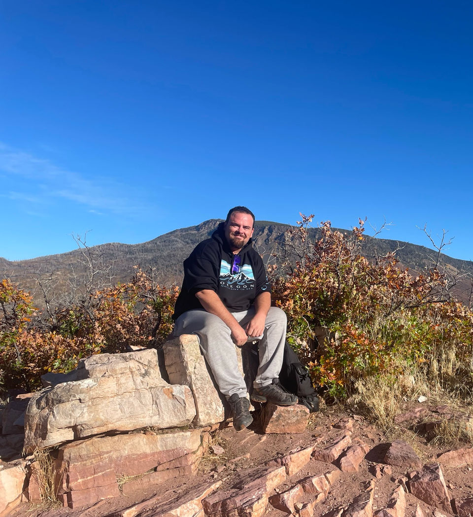 Smiling man on red rock with mountains and fall trees