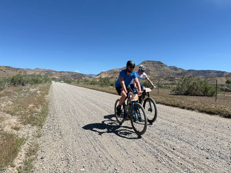 Two cyclists riding on a gravel road with hills in the background