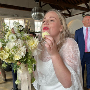 a woman in a white dress is eating cheese and  holding a bouquet of flowers and eating a piece of cheese