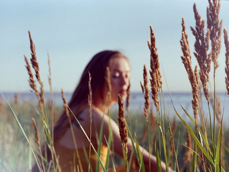 a woman sits in a green hill, behind the wheat