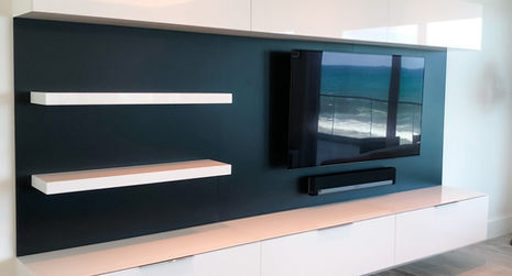 Modern white entertainment center with dark blue wall and a large TV.