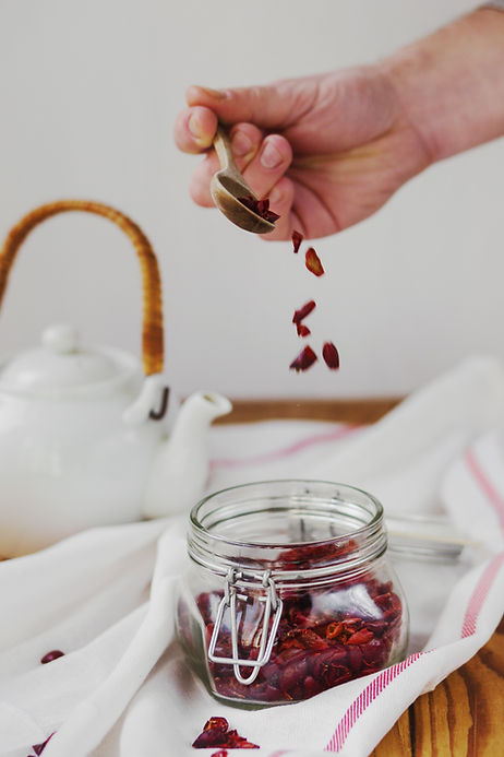 Small pieces of dried fruit being poured from a spoon into a glass Jar.