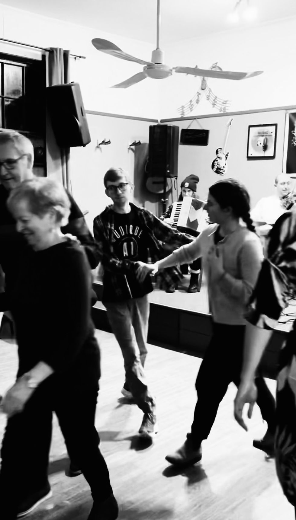 People dancing in a hall with musicians in the background. The mood is lively and joyful.