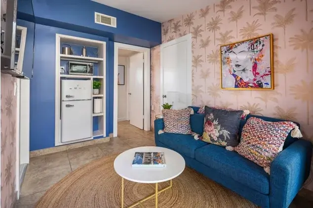 Studio apartment with blue accent wall, botanical pink wallpaper, and blue sofa in Palm Springs boutique hotel