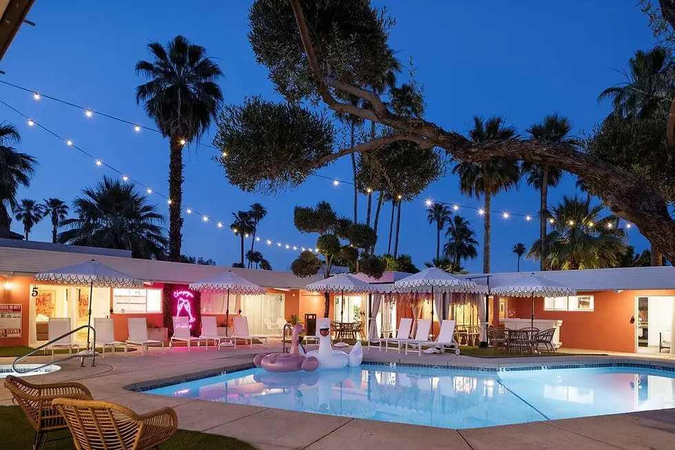 Illuminated resort pool at dusk with orange bungalows, string lights, and palm trees