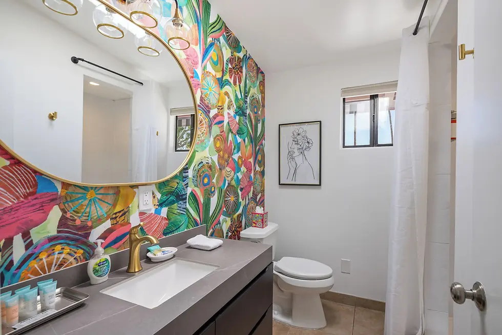 Contemporary bathroom with psychedelic floral wallpaper, brass mirror, and modern black vanity at The Muse Hotel Palm Springs