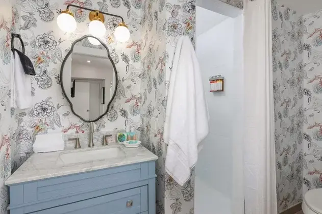 Floral wallpaper bathroom with blue vanity and marble countertop in Palm Springs boutique hotel suite