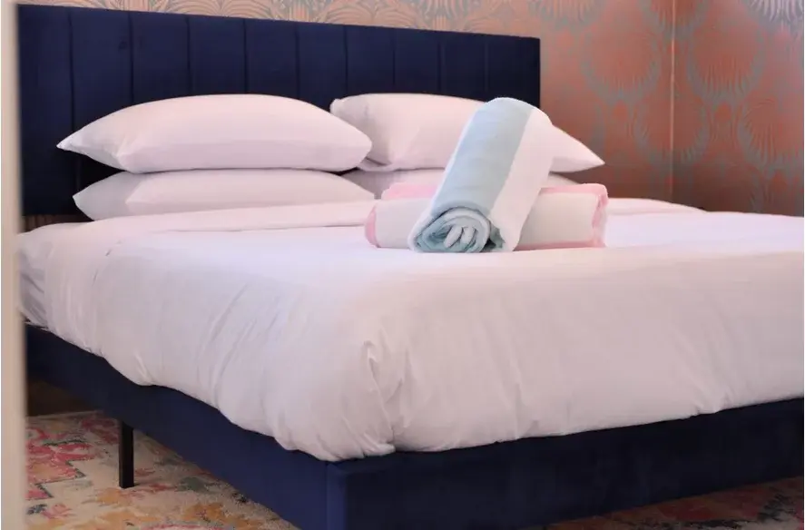 Romantic hotel suite bedroom with navy headboard, coral patterned wallpaper, white linens at The Muse Hotel Palm Springs