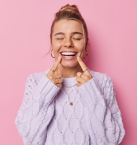 Fröhliche Frau zeigt mit Fingern auf Mund, wo man ihre obere und untere Zahnreihe sieht