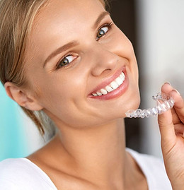 Junge Frau lächelt und hält durchsichtige lose Zahnspange für Zähne in der Hand