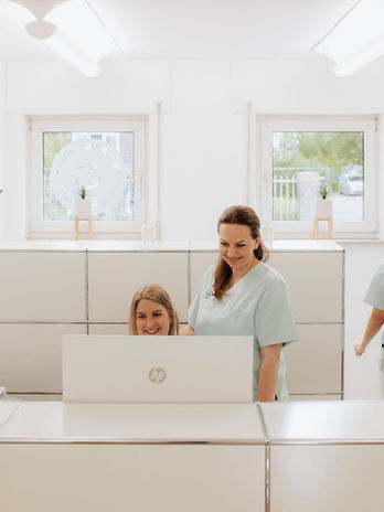 Zwei Mitarbeiterinnen hinter dem Empfangstresen arbeiten. KFO Hofmayer, helle und freundliche Praxis in Dortmund Hörde