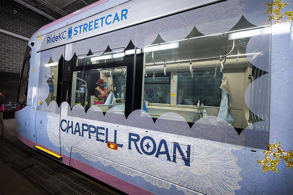 Streetcar decorated with "Chappell Roan" text and lace patterns. Person in safety vest inside, background shows a brick wall.