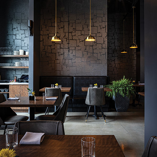 Modern restaurant Urban interior with dark booths, wooden tables, and gold pendant lights. Beige walls, ferns, and a serene, elegant atmosphere.