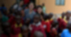 Volunteers pose with smiling children in Uganda Schools, wearing red uniforms.