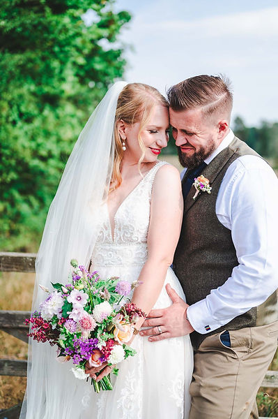 A bride and groom wearing a waistcoat lean into each other against a gate at Elmhay Park, Frome, Somerset