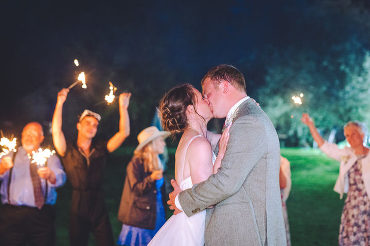 Bride and groom sharing a romantic kiss surrounded by guests holding lit sparklers in the darkness at a Wiltshire wedding