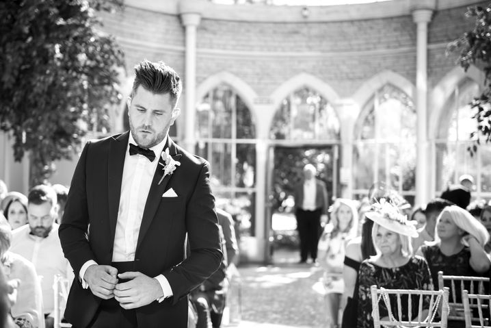 Black and white photo of a nervous groom waiting at the altar in the stunning glass orangery at Tortworth Court, Gloucestershire