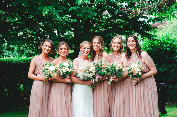 Bride with four bridesmaids in blush pink dresses holding wildflower bouquets in the gardens at a marquee wedding