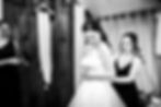 Bride in wedding dress being helped with final adjustments by bridesmaid during getting ready time before the ceremony