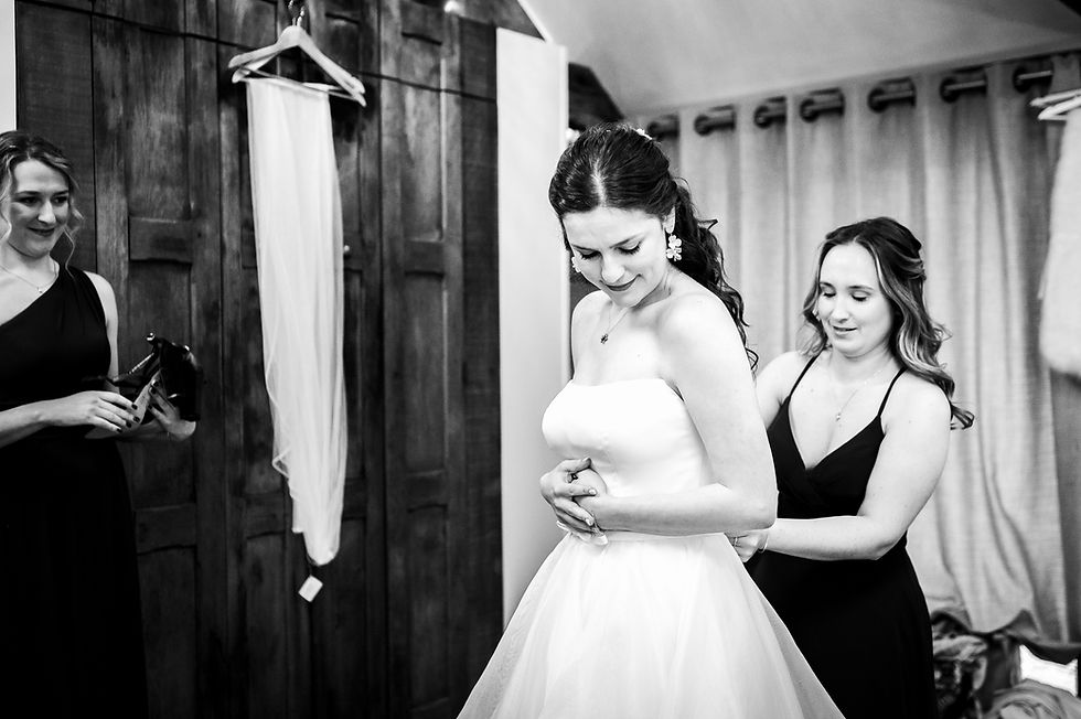 Bride in wedding dress being helped with final adjustments by bridesmaid during getting ready time before the ceremony