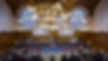 A view of the court at the International Court of Justice. A blueish floor carpet, the 15 Judges at a raised table, 2 big T V screens displaying the court's proceedings, and many seats for the plaintifs.
