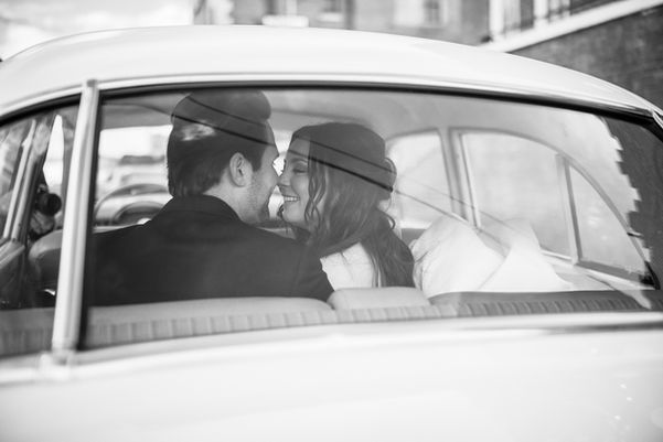 black and white image of bride and groom kissing in back seat of vintage car