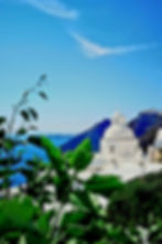 White dome in Santorini framed by green leaves with blue sea background