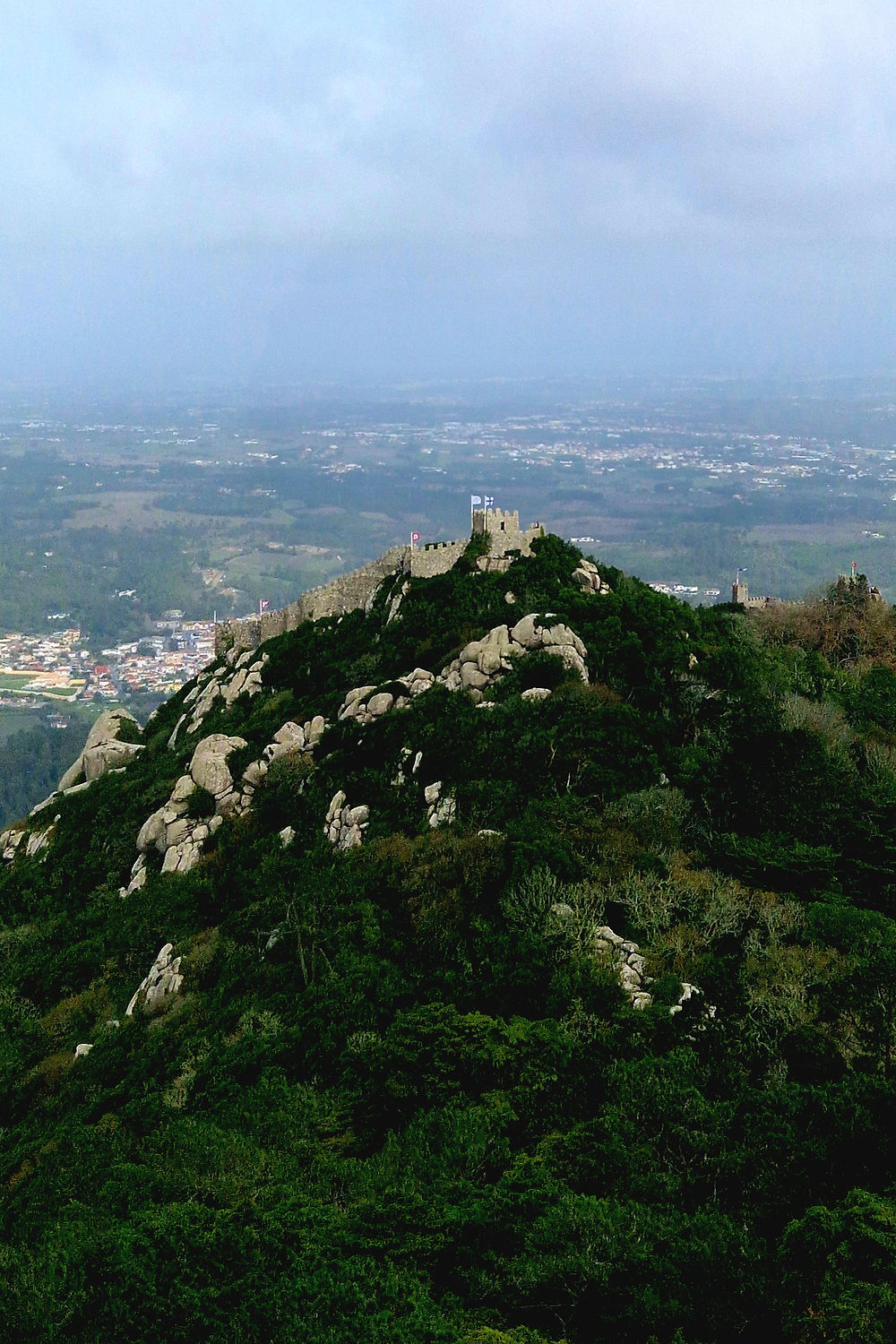 View of the Moorish Castle in Sintra, Portugal, on a hill surrounded by forest and light haze