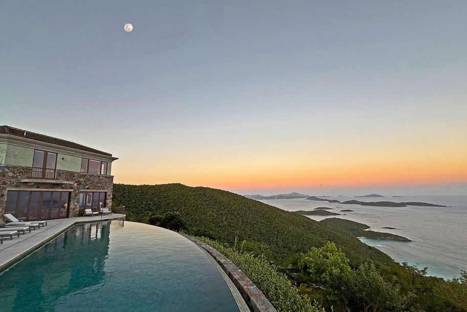 Infinity pool overlooking ocean with green hills and a beautiful sunset