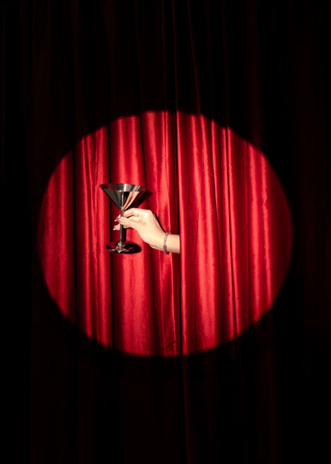 Ręka trzymająca kieliszek do martini na tle czerwonej aksamitnej kurtyny w świetle reflektora — stylowa scenografia glamour w studiu fotograficznym ONEGOG Creative Space w Gdańsku, idealna do sesji kreatywnych i contentu UGC.