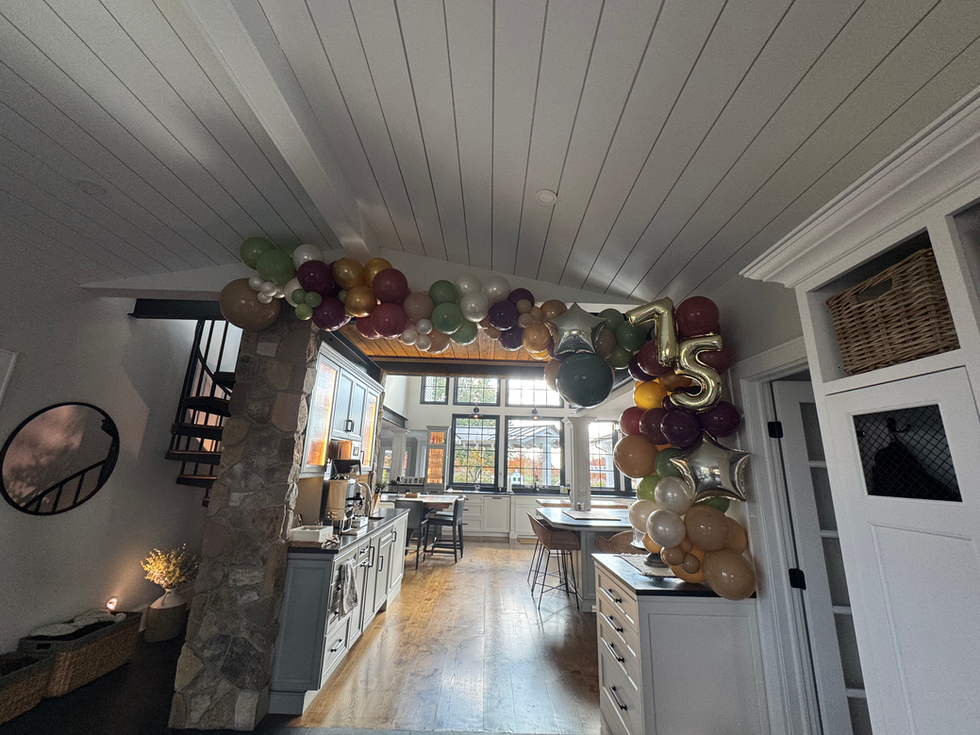 Party room with green and brown balloon arch, gold '75'