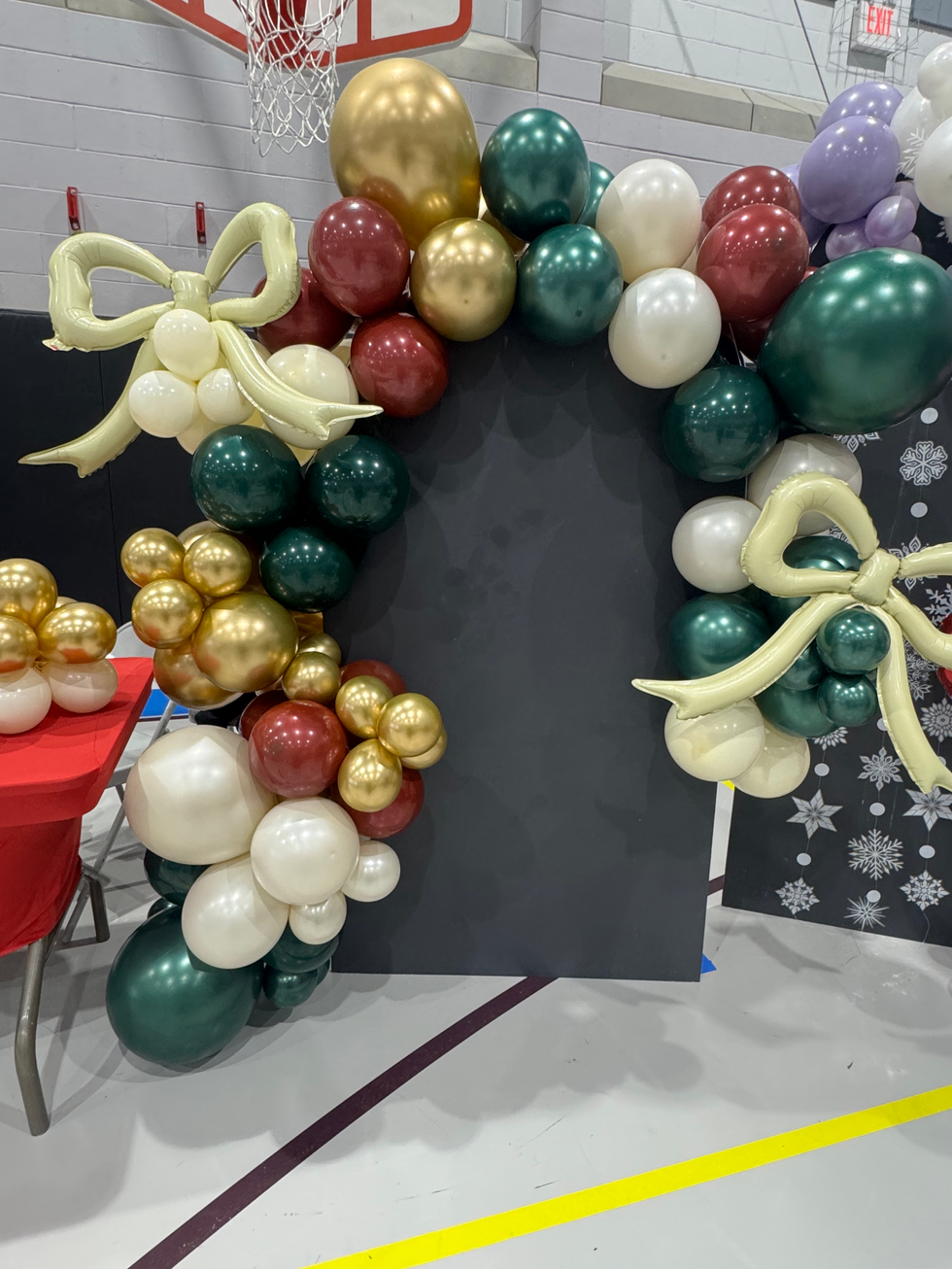 Holiday balloon arch with red, gold, green, cream balloons and bows