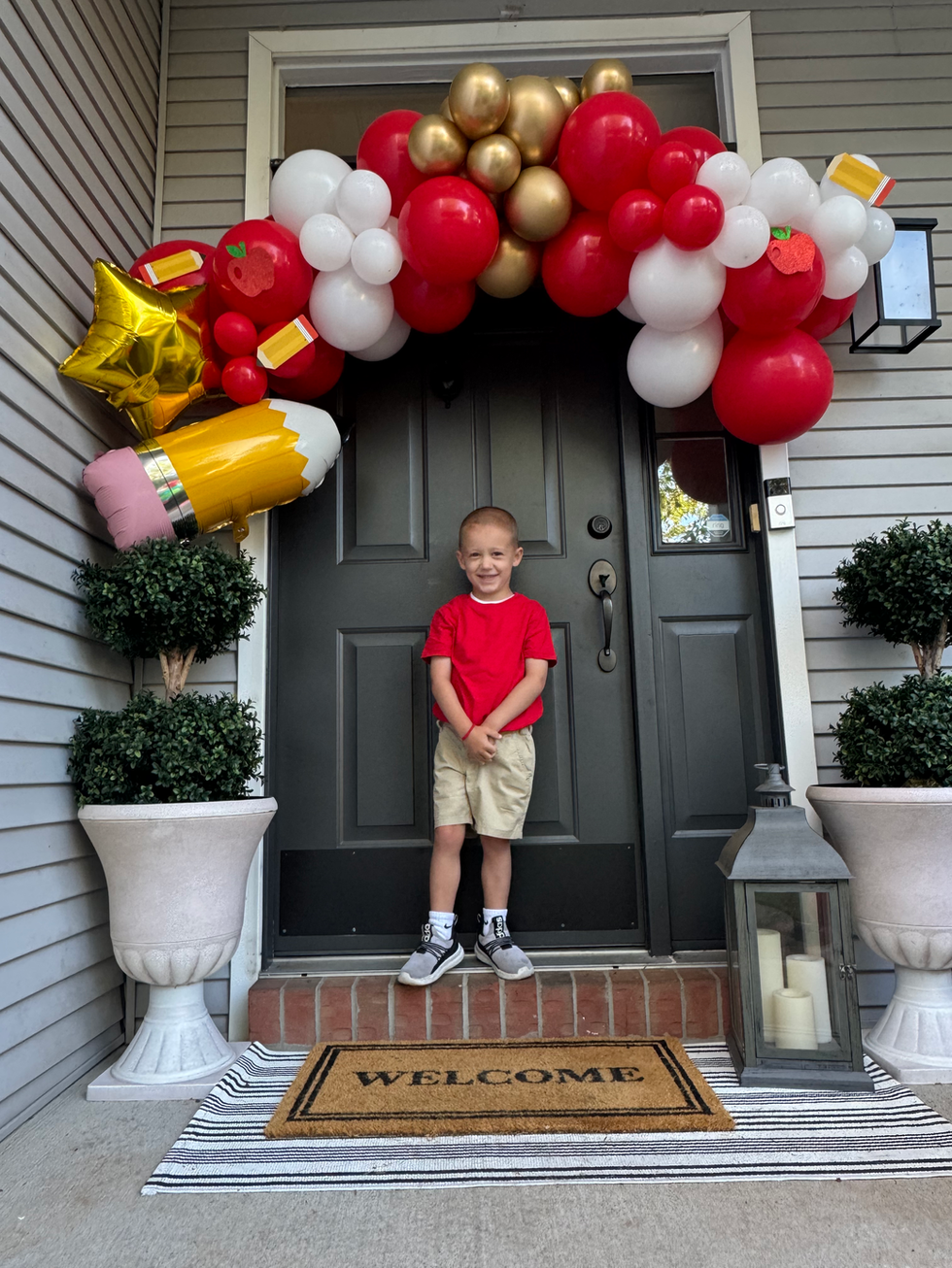 Boy in red shirt by door decorated with balloons and pencil balloon