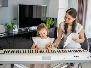 家庭的な環境で、講師が子どもの手を添えてピアノを丁寧に指導している場面。
