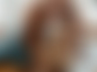 Woman in an orange sweater cuddles a golden retriever by a bright window, both calm and affectionate.