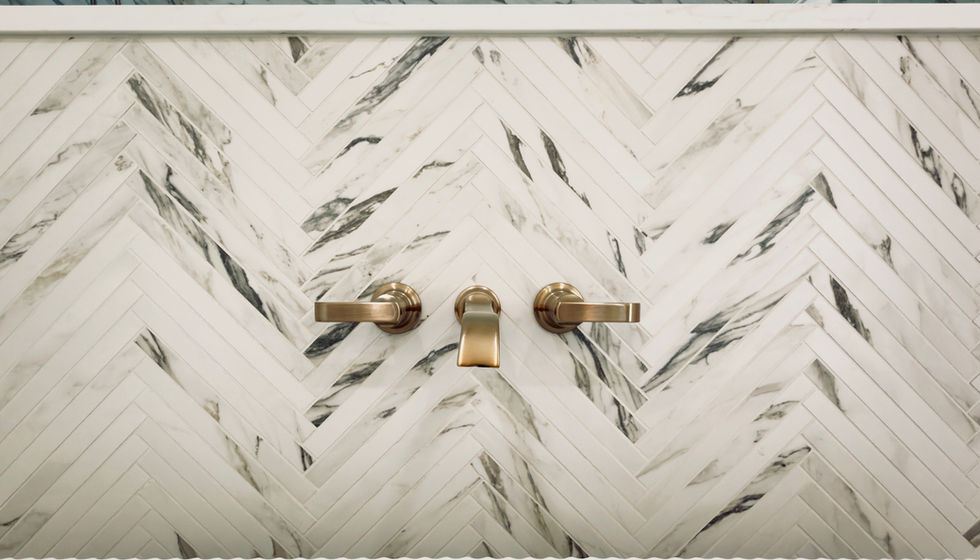 Detail of herringbone-pattern marble tile accent wall behind a freestanding tub with wall-mounted brass tub filler in a modern luxury bathroom.