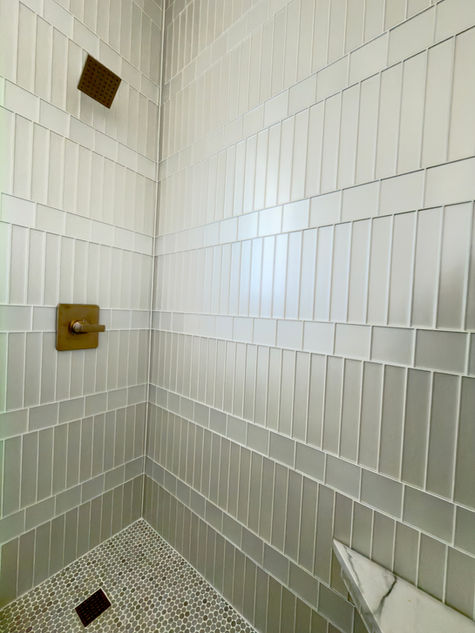 Walk-in shower featuring vertically stacked pearl glass tile walls, brass shower fixtures, and a penny tile shower floor.