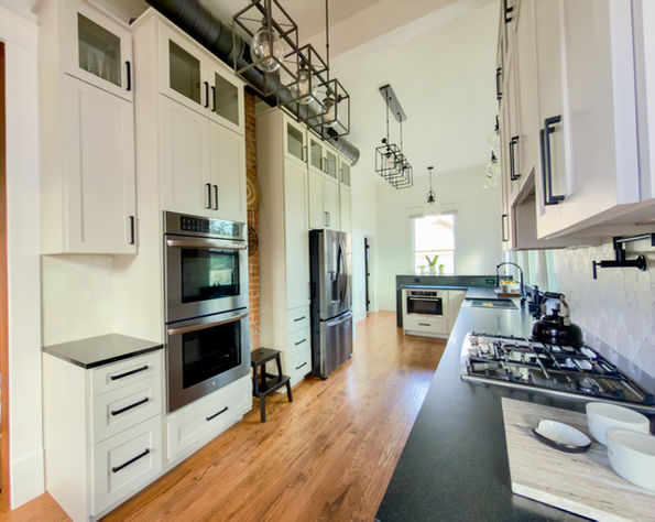 Galley kitchen renovation in a historic home, featuring stone colored cabinetry, black natural stone countertops, statement lighting, and matte black fixtures with warm wood flooring