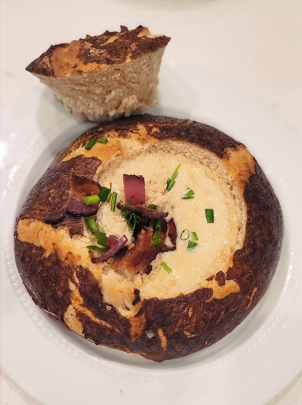 Pretzel bowl with center filled with beer cheese soup with bacon and chive garnish.