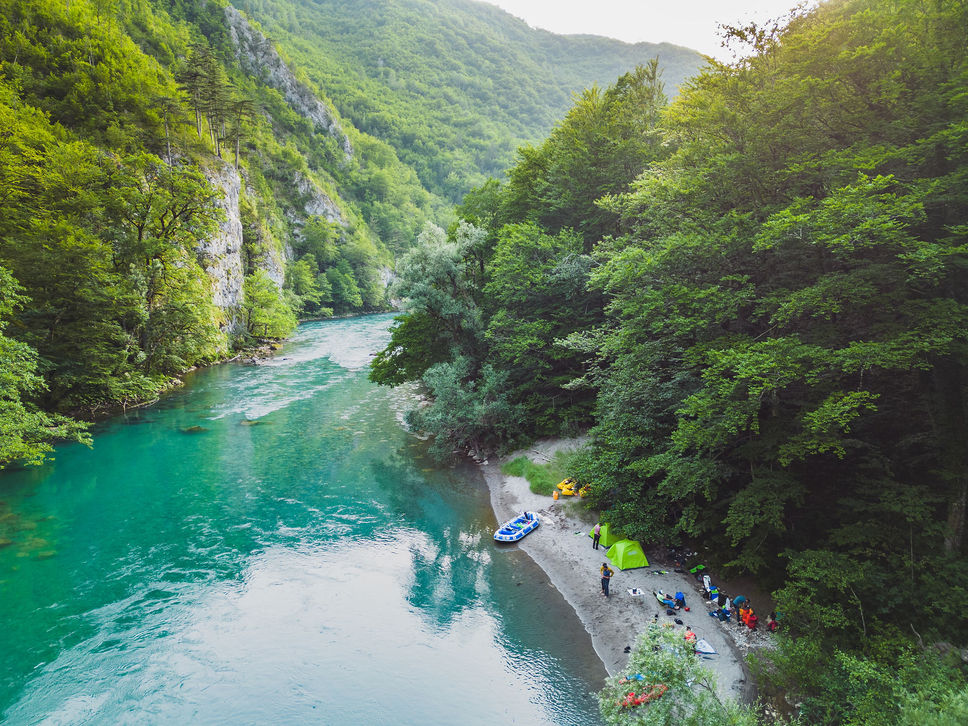 Aerial view of a remote riverside campsite surrounded by forested canyon walls in Montenegro