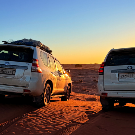 Expedition vehicles at sunrise in the Sahara.